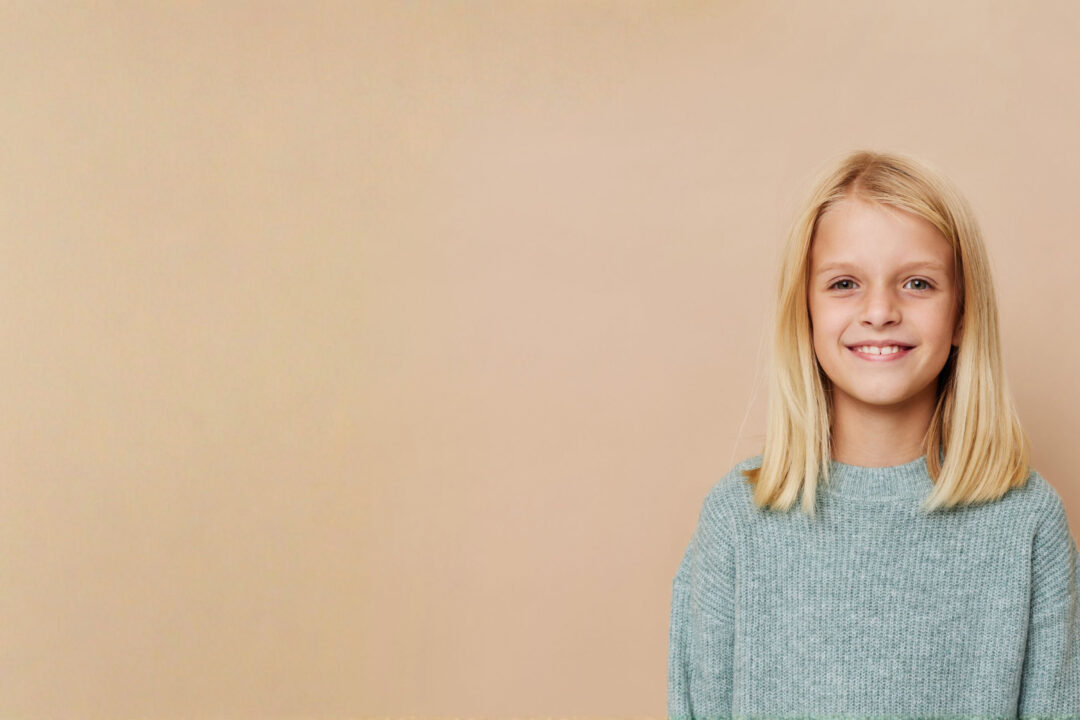 Kinderfriseur in Erlangen - Haarmacherei in Erlangen, Bayern - Hübsches blondes Mädchen mit schönen blonden Haaren vor peachfarbigen Hintergrund